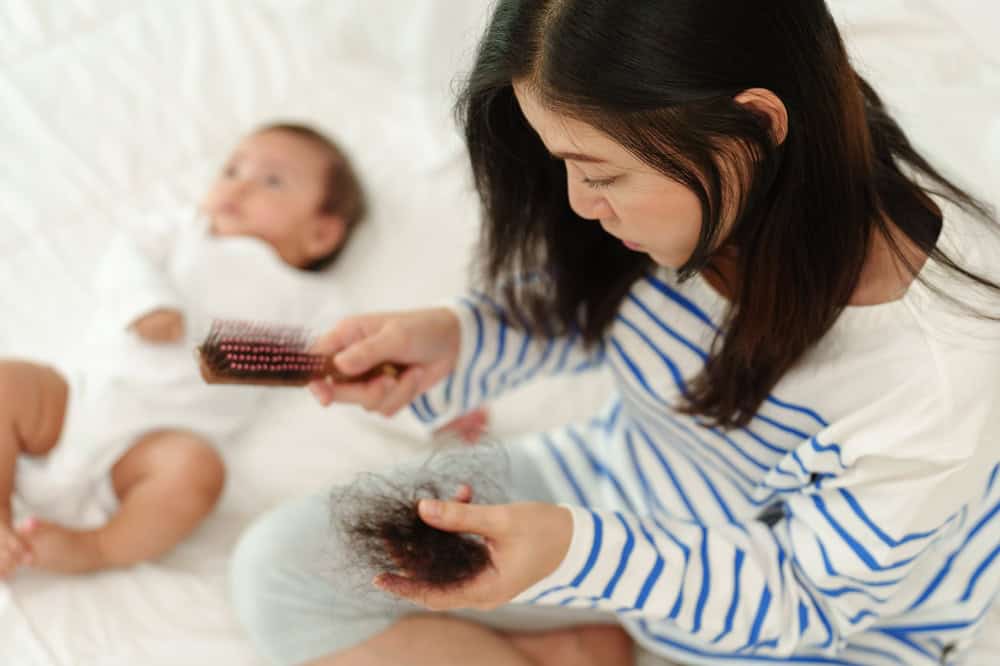 A mother holding shed hair, a common sign of postpartum hair loss