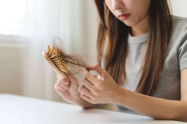 Woman noticing diffuse hair shedding while brushing, an early sign of telogen effluvium.