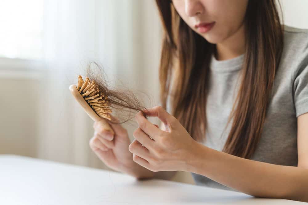 Woman noticing diffuse hair shedding while brushing, an early sign of telogen effluvium.