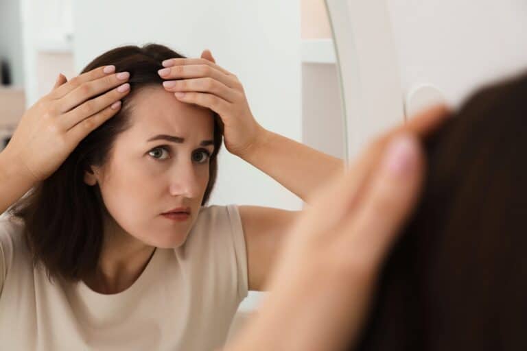 A woman checking her hair in the mirror, with early androgenetic alopecia female patterns present.