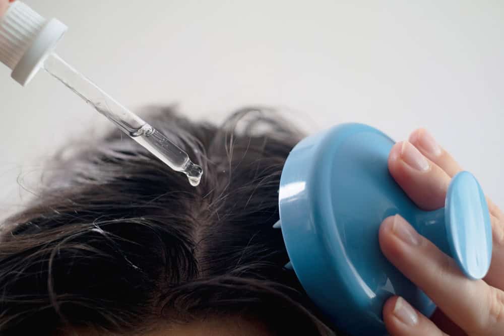 An individual applying topical scalp treatment after taking vitamins for hair growth and thickness.