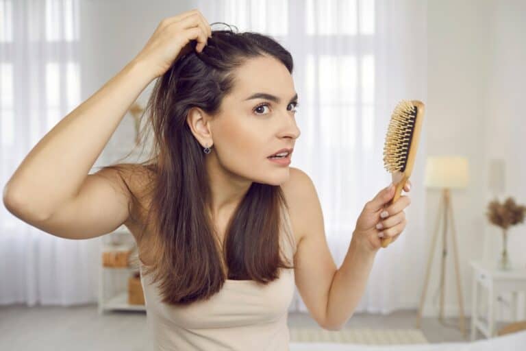 Woman examines her scalp for thinning, a common reason to explore hair loss therapy