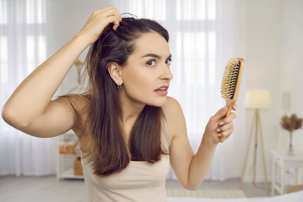 Woman examines her scalp for thinning, a common reason to explore hair loss therapy