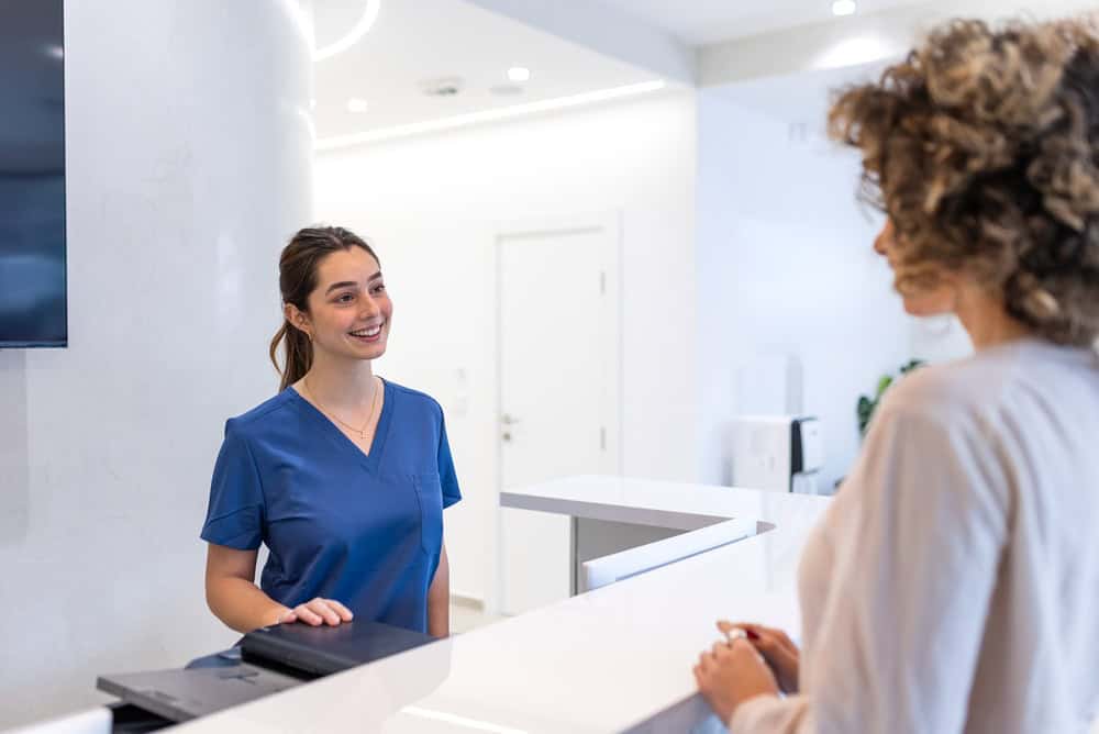 Medical clinic receptionist greeting a patient during check-in for a consultation